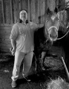 A black and white photo of a man standing next to a horse.